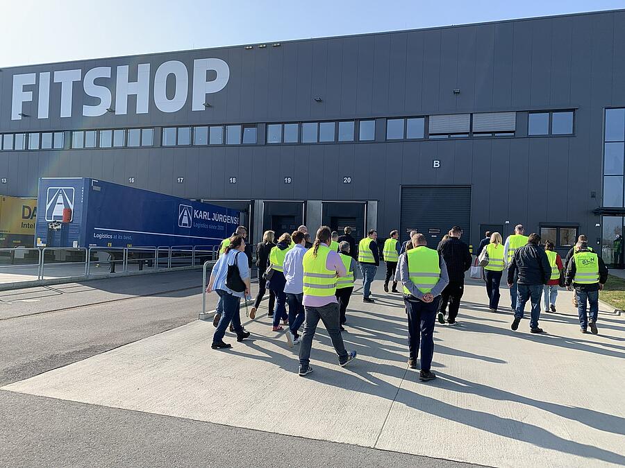 Viele Menschen in gelben Westen gehen auf ein großes Logistikzentrum zu.