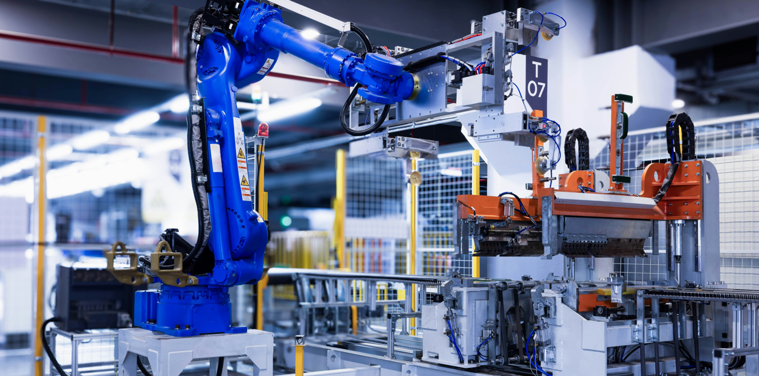 Eine Fabrikhalle in der man einen Roboterarm in der Produktion sieht.