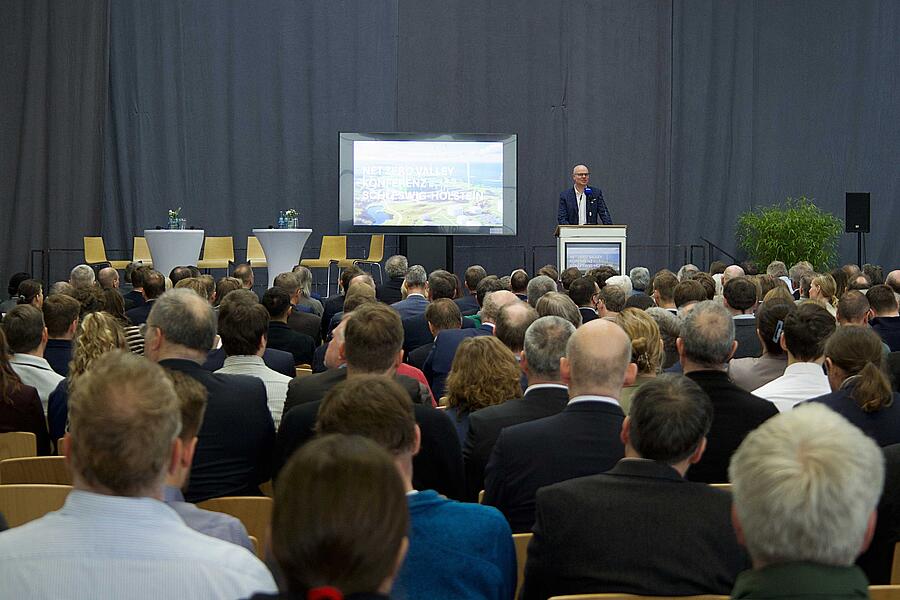 Mann am Rednerpult, davor das Publikum sitzend.