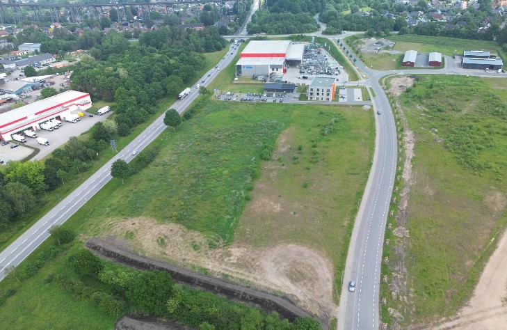 Luftbild eines Gewerbegebiets. Im Vordergrund eine freie Fläche, im Hintergrund Geberbeimmobilien.