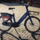Foto eines E-Bikes der Kieler Sprottenflotte. Blaues Fahrrad mit Aufdruck "Sprottenflotte" und Werbeschild am Gepäckträger. Das Fahrrad steht auf Kopfsteinpflaster.
