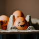 Eierkarton mit drei Eiern, die mit Gesichtern bemalt wurden.