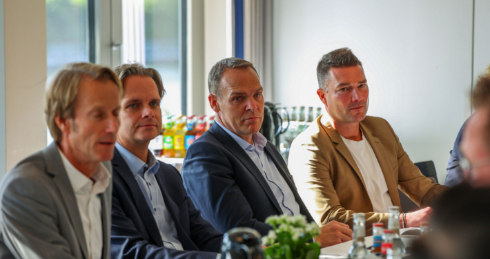 Vier Männer im Anzug, die nebeneinander an einem Tisch sitzen.